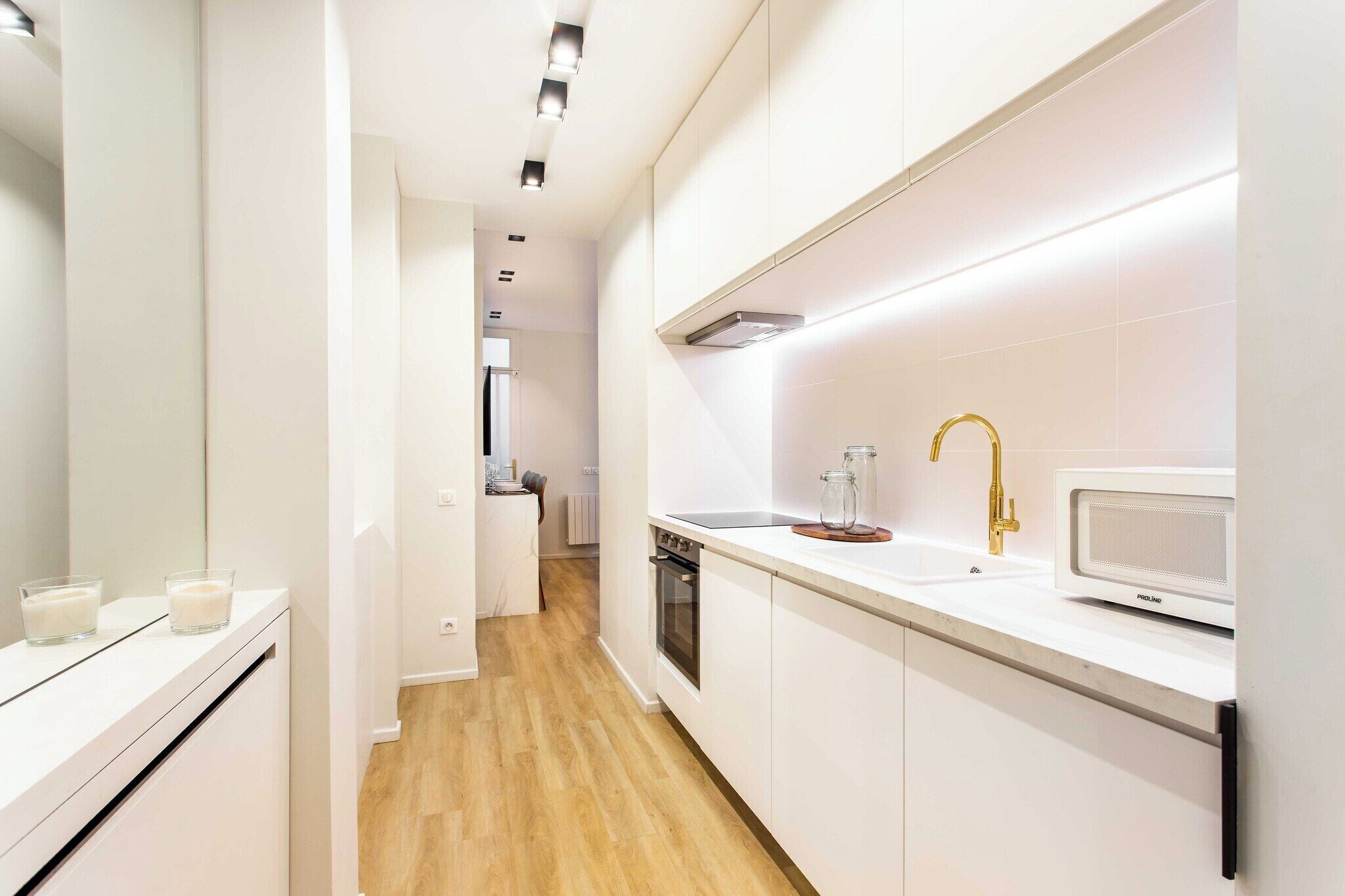 Eine moderne Küche mit weißen Schränken, einer Mikrowelle, einem Waschbecken mit Goldarmatur und einem Glas auf der Arbeitsplatte.