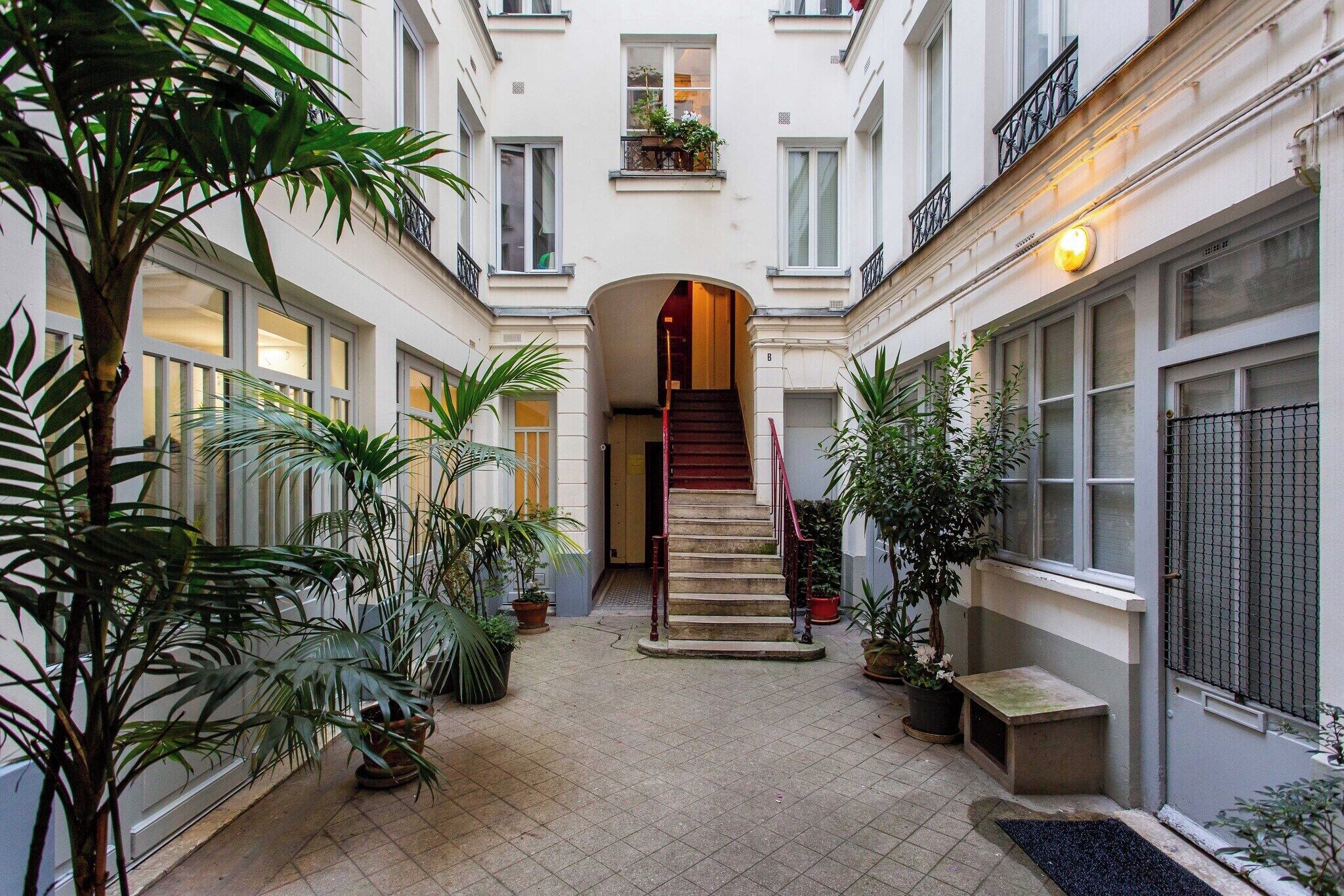 Un cortile con una scalinata centrale, piante in vaso e una panchina.