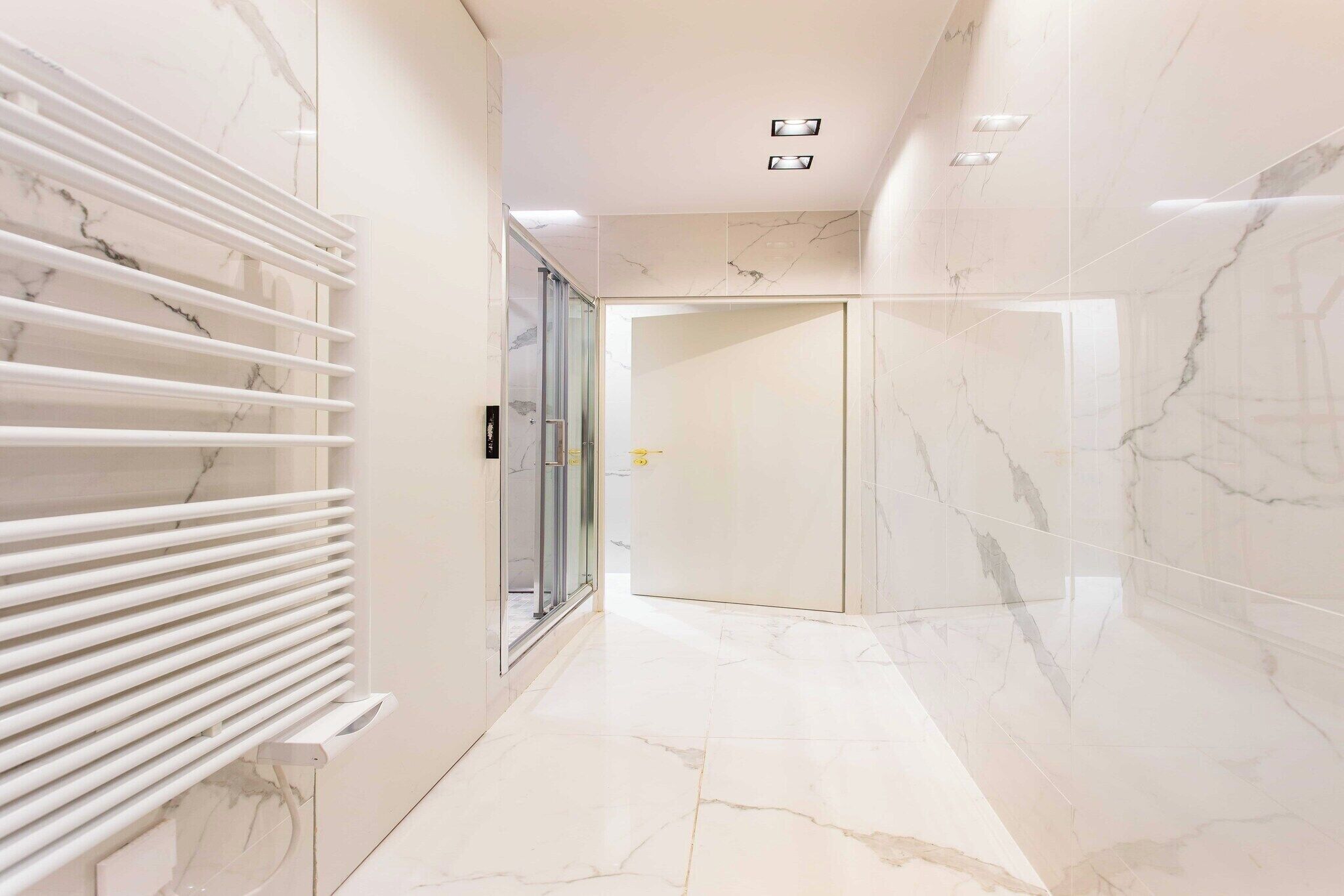 Un corridoio con pavimento in marmo e pareti decorate, una porta in vetro e un termosifone bianco.