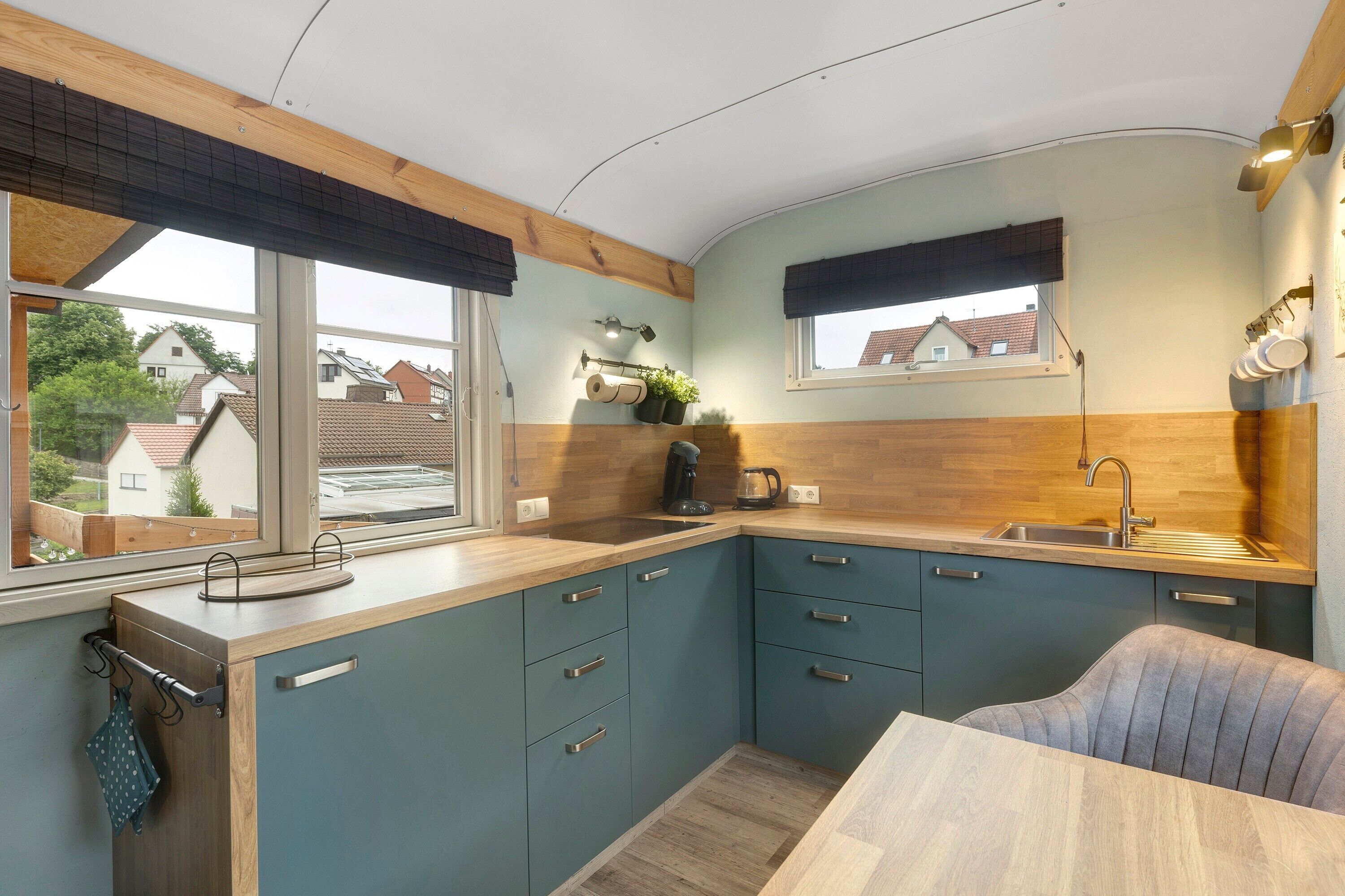 A compact kitchen with a window, wooden ceiling, and teal cabinetry.