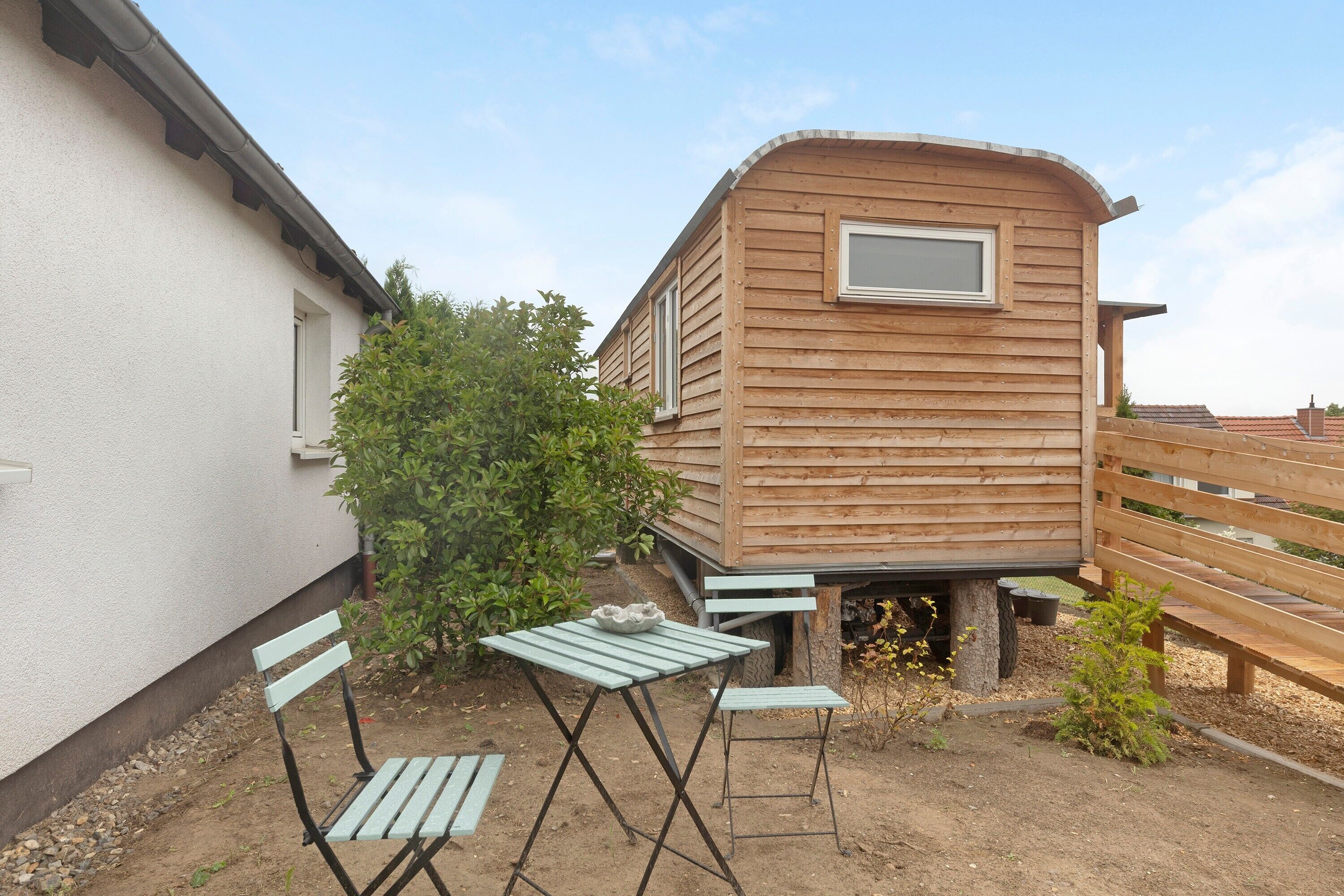 Una casa móvil de madera con ventana, una mesa y dos sillas en un jardín.
