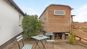 Una casa móvil de madera con ventana, una mesa y dos sillas en un jardín.