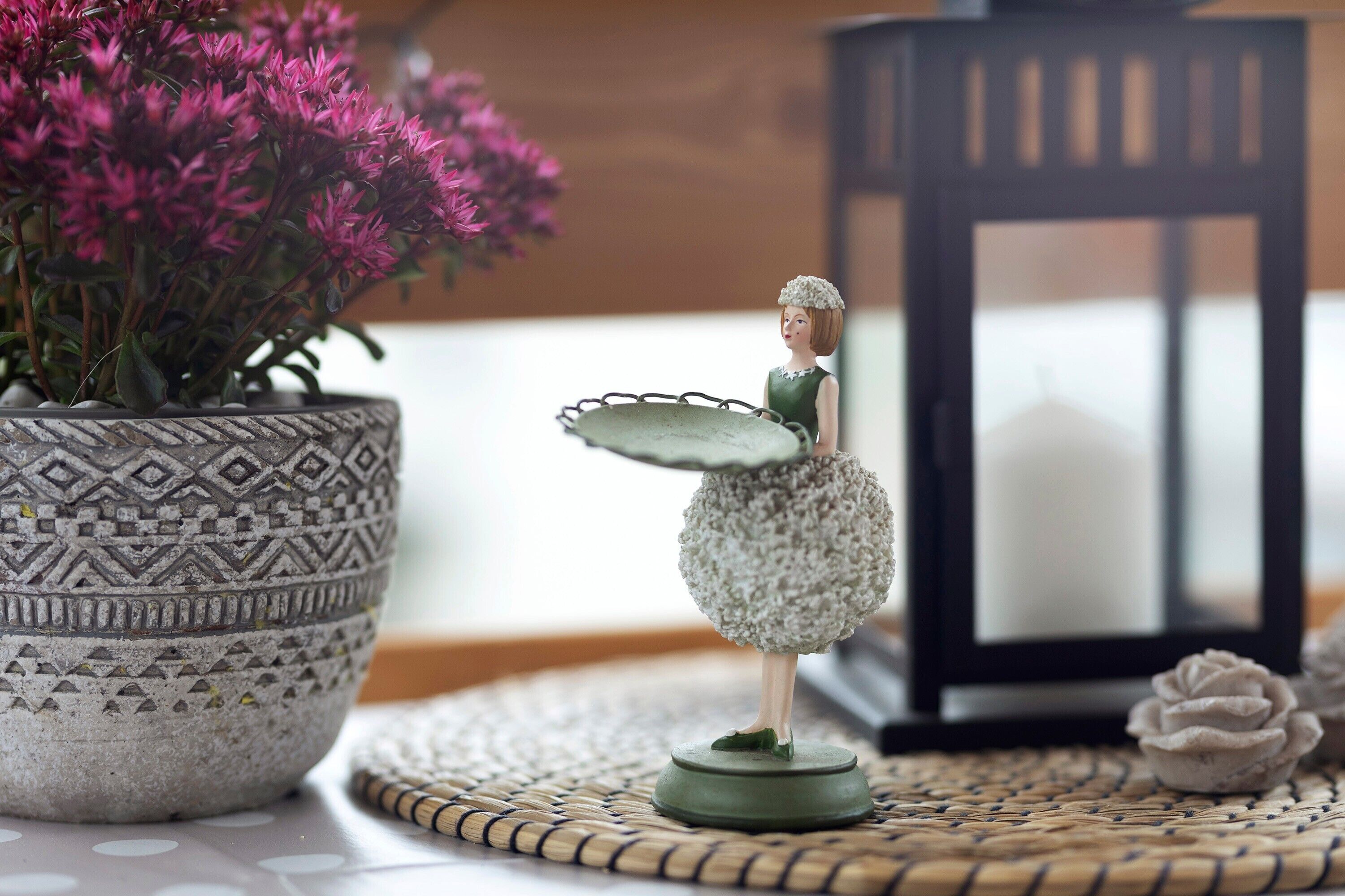 A figurine on a table with a patterned pot and a candle in the background.