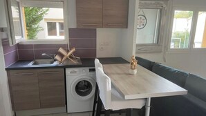 A compact kitchen with a built-in washing machine, a dining table, and a green sofa. - T2 apartment with terrace, not overlooked, 3' from la Ramée leisure park (Tournefeuille)