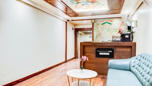 A reception area with a wooden reception desk, a sofa, a small table with a vase, and a ceiling with a floral design. - Townhouse Oak Viman Nagar Hotel Cilantro (Pune)