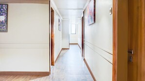 A long, narrow hallway with wooden flooring and white walls, leading to a door on the right. - Townhouse Oak Viman Nagar Hotel Cilantro (Pune)