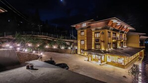 A multi-story building with a balcony and a covered area, surrounded by a landscaped garden with lights. - Paro Heritage Hotel (Paro)
