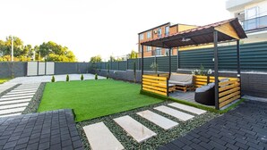 En moderne udendørs terrasse med træterrasse, overdækket siddeområde og velplejet græsplæne.