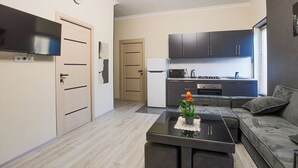En moderne stue med et fladskærms-tv, et sofabord med en pynteting, en sofa og et køkkenområde med skabe og hårde hvidevarer.
