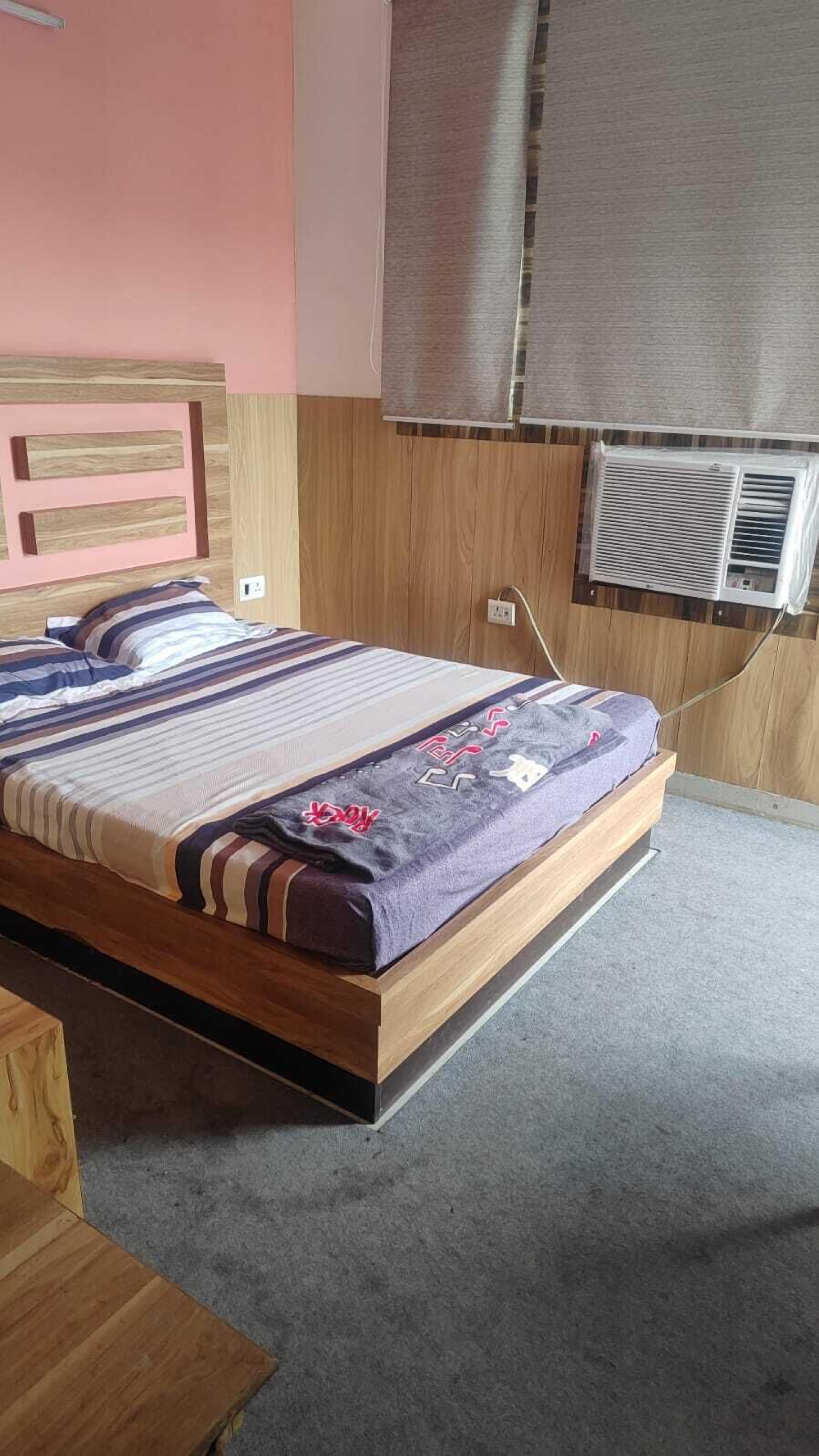 Una cama individual con estructura y cabecera de madera, una mesita de noche y un equipo de aire acondicionado instalado en la pared.