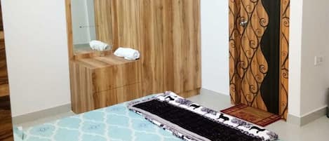 A bedroom with a bed, a wooden wardrobe, a mirror, and a patterned curtain.