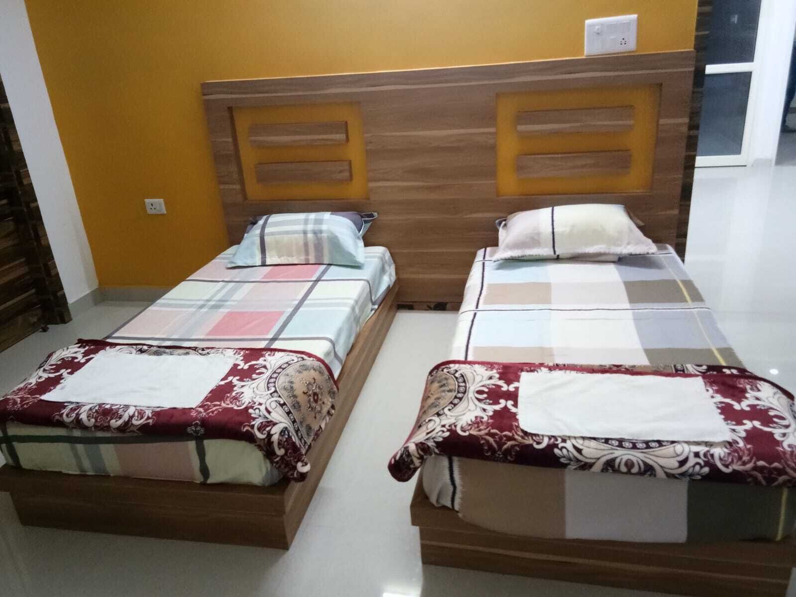 Two single beds with wooden headboards, a plain wall, and a door in the background.