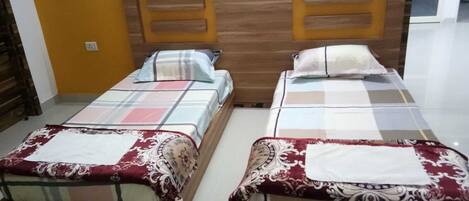 Two single beds with wooden headboards, a plain wall, and a door in the background.