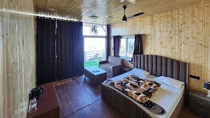 A bedroom with a wooden ceiling, a bed with a patterned bedspread, a nightstand, a chair, and a window with curtains. - Perrys Cottage (Tehri)