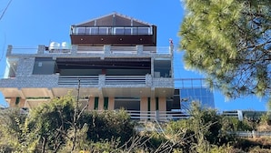A modern multi-story building with a flat roof, large windows, and a balcony on the upper floor. - Perrys Cottage (Tehri)