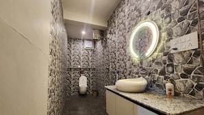 A bathroom with a stone wall, a toilet, a sink with a mirror, and a countertop with toiletries. - Perrys Cottage (Tehri)