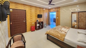 A modern hotel room with a wooden wall, a bed with patterned bedding, a ceiling fan, a TV, and a wardrobe. - Perrys Cottage (Tehri)