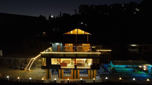 A multi-story building with a central atrium, a covered outdoor area with seating, and a pool. - Perrys Cottage (Tehri)