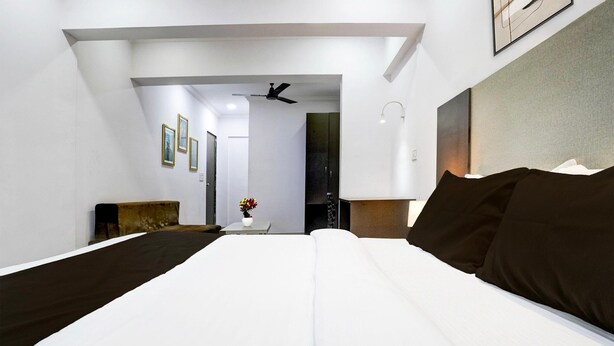 A hotel room with a large bed, a ceiling fan, a small table with a vase of flowers, and a view of the hallway.