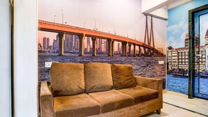 A room with a large window, a brown sofa, and a mural of a bridge and cityscape.