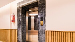 An elevator with a marble wall, a fire extinguisher, and a wooden paneling floor. - Palette Shree Jagannath Puri (Puri)