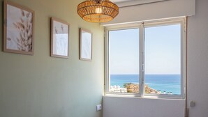 A bedroom with a large window offering a view of the sea, a bed with striped bedding, and two framed pictures on the wall. - Paradise View (Villajoyosa)