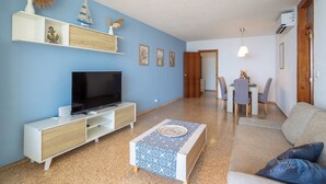 A modern living room with a flat-screen TV, a coffee table, and a sofa. There is a dining area with a table and chairs. - Paradise View (Villajoyosa)