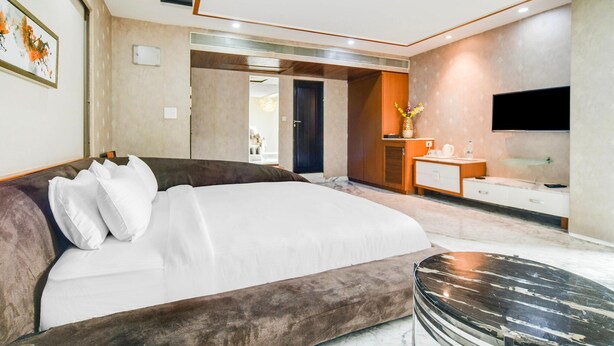 A modern bedroom with a large bed, a vanity with a mirror, and a flat-screen TV mounted on the wall. - Palette Sapphire Star (Indore)