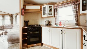 A compact kitchen with a stove, oven, cabinets, and a window with curtains.