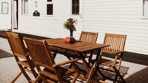A wooden table and chairs set outside a white building with windows and doors.
