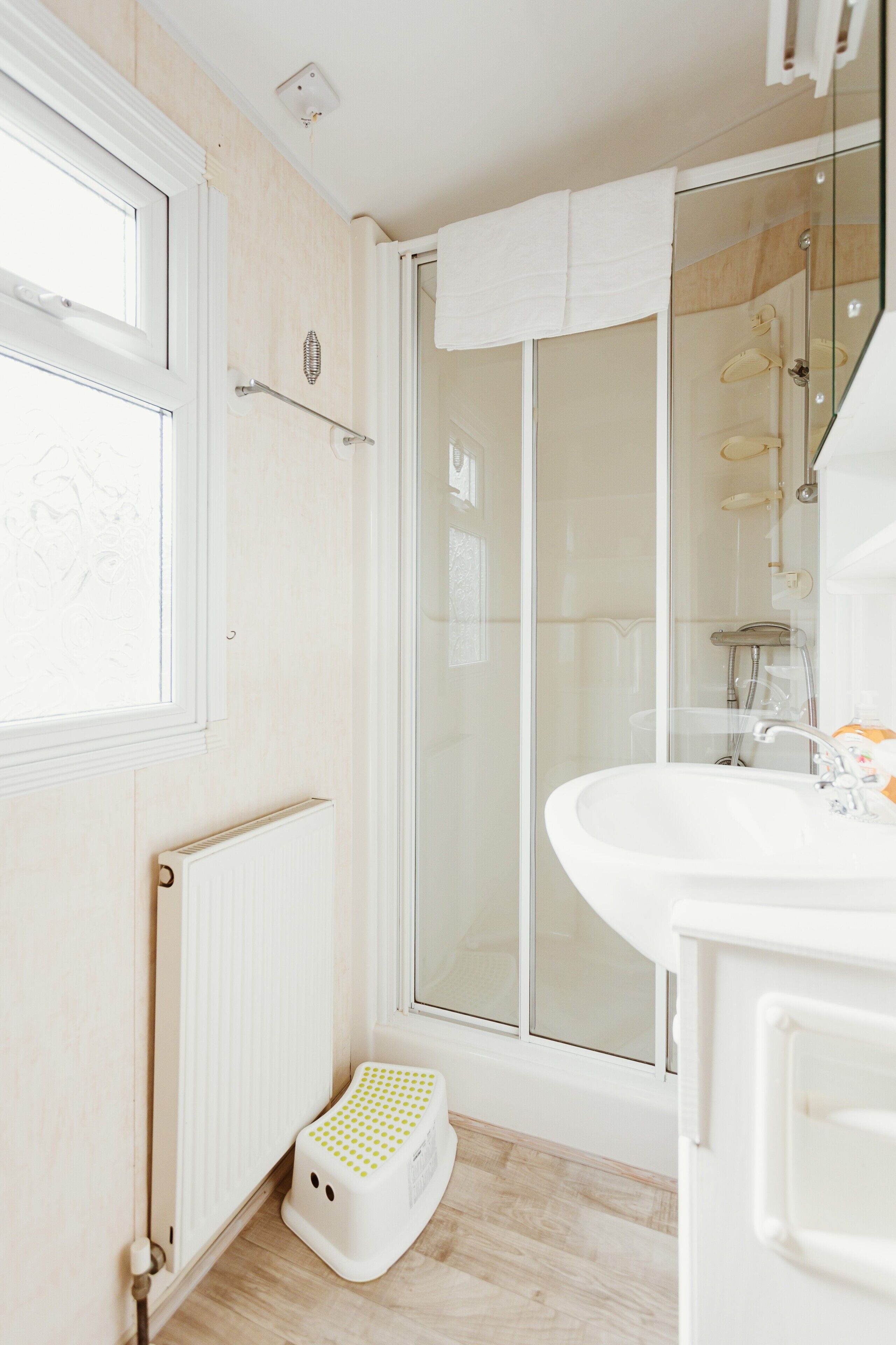 Une salle de bain avec une douche à parois de verre, un lavabo blanc et un petit marchepied.