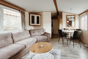 A modern living room with a sofa, a round wooden coffee table, and a dining area with chairs and a table.