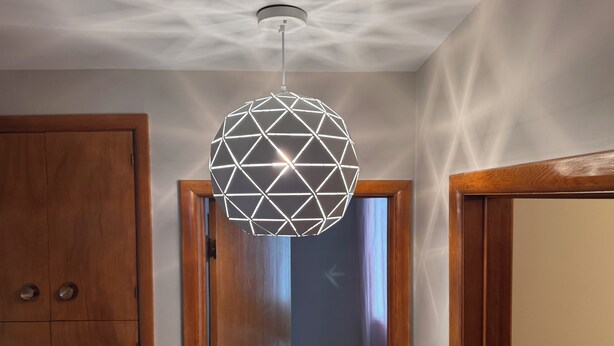 Un couloir agrémenté d’un luminaire suspendu aux formes géométriques, de portes en bois et d’un plafond au motif texturé.
