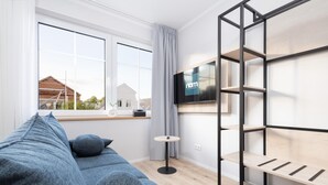 Una sala de estar moderna con un sofá gris, un televisor montado en un marco de metal negro y un ventanal con vista a una casa.