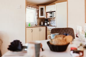 Una cucina compatta con forno a microonde, macchina del caffè e una finestra con tende.
