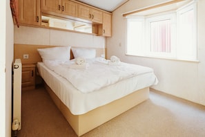 Un dormitorio con cama, armarios de madera, una ventana y un radiador.