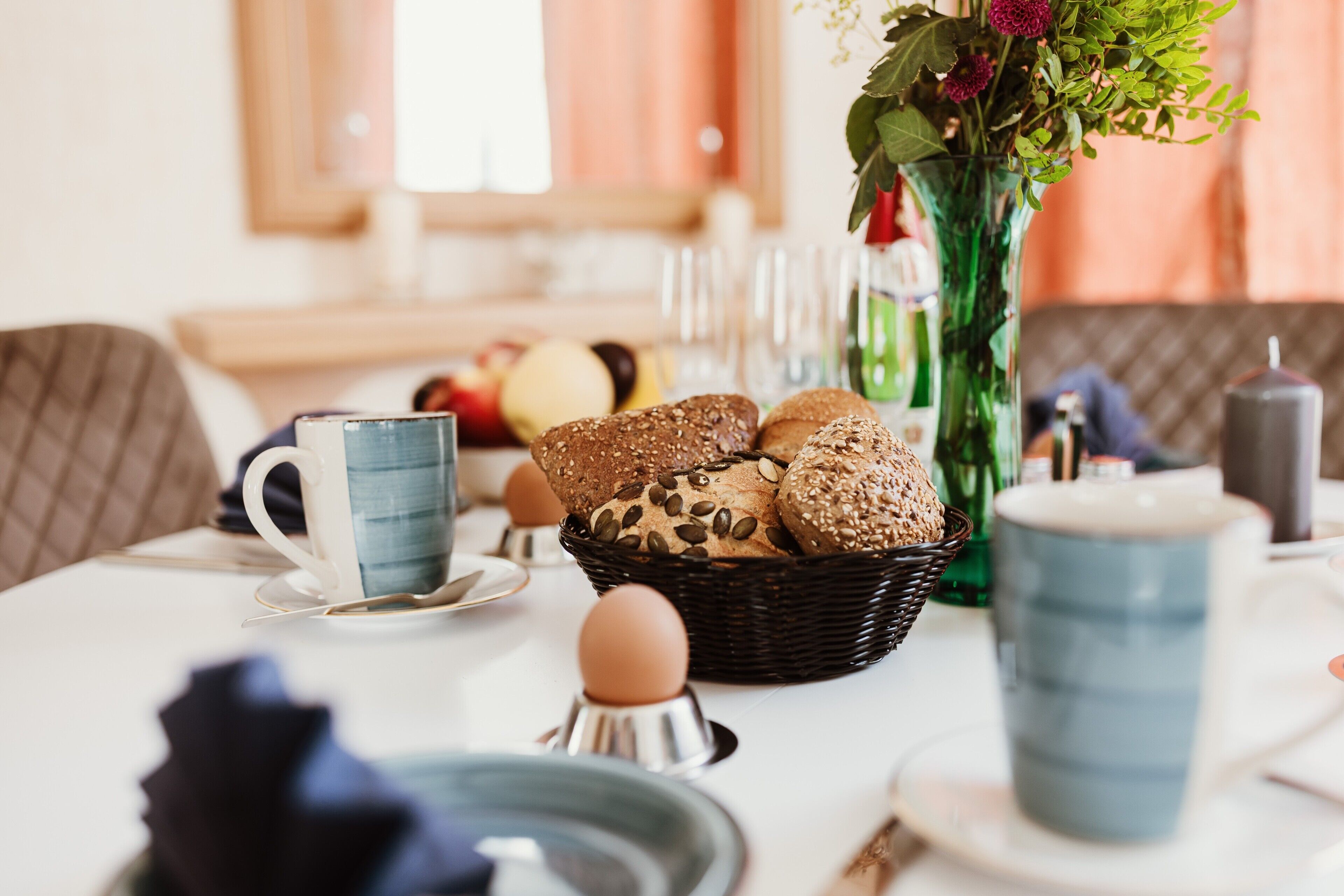 Ein Esstisch mit einem Brotkorb, einer Blumenvase und einer blauen Tasse.