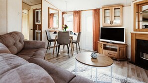 Een woonkamer met een bank, een eettafel, stoelen, een televisie en houten kasten.