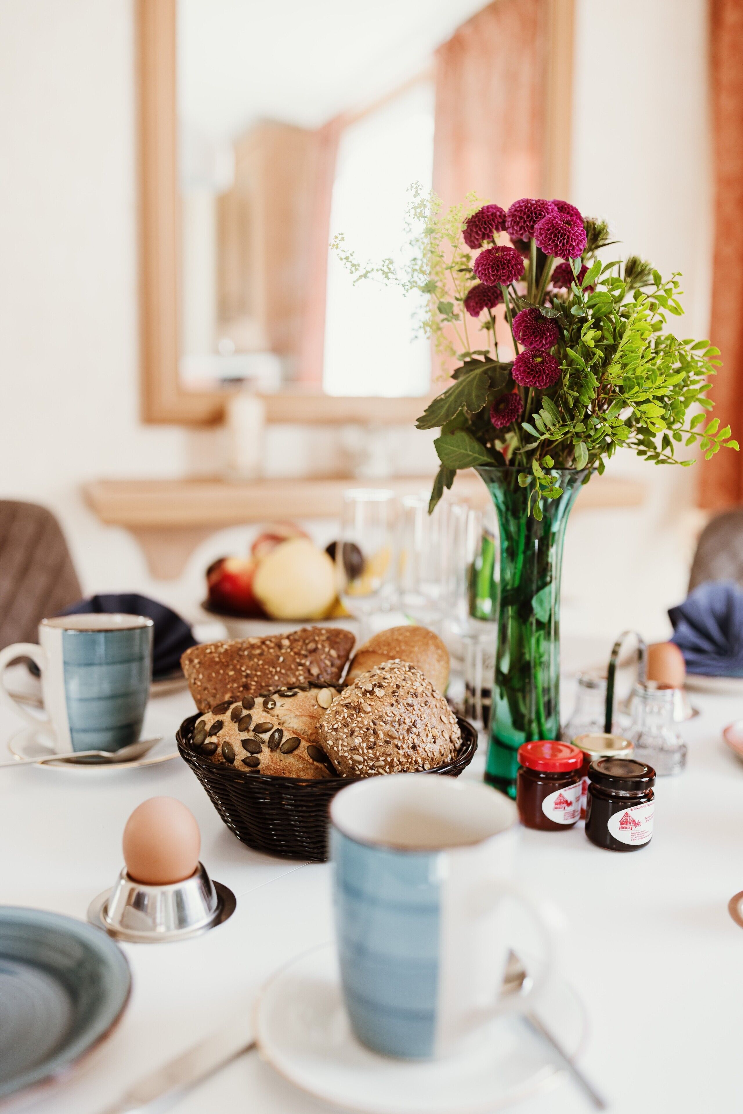 Uma mesa de café da manhã com pão, ovos e um vaso de flores.