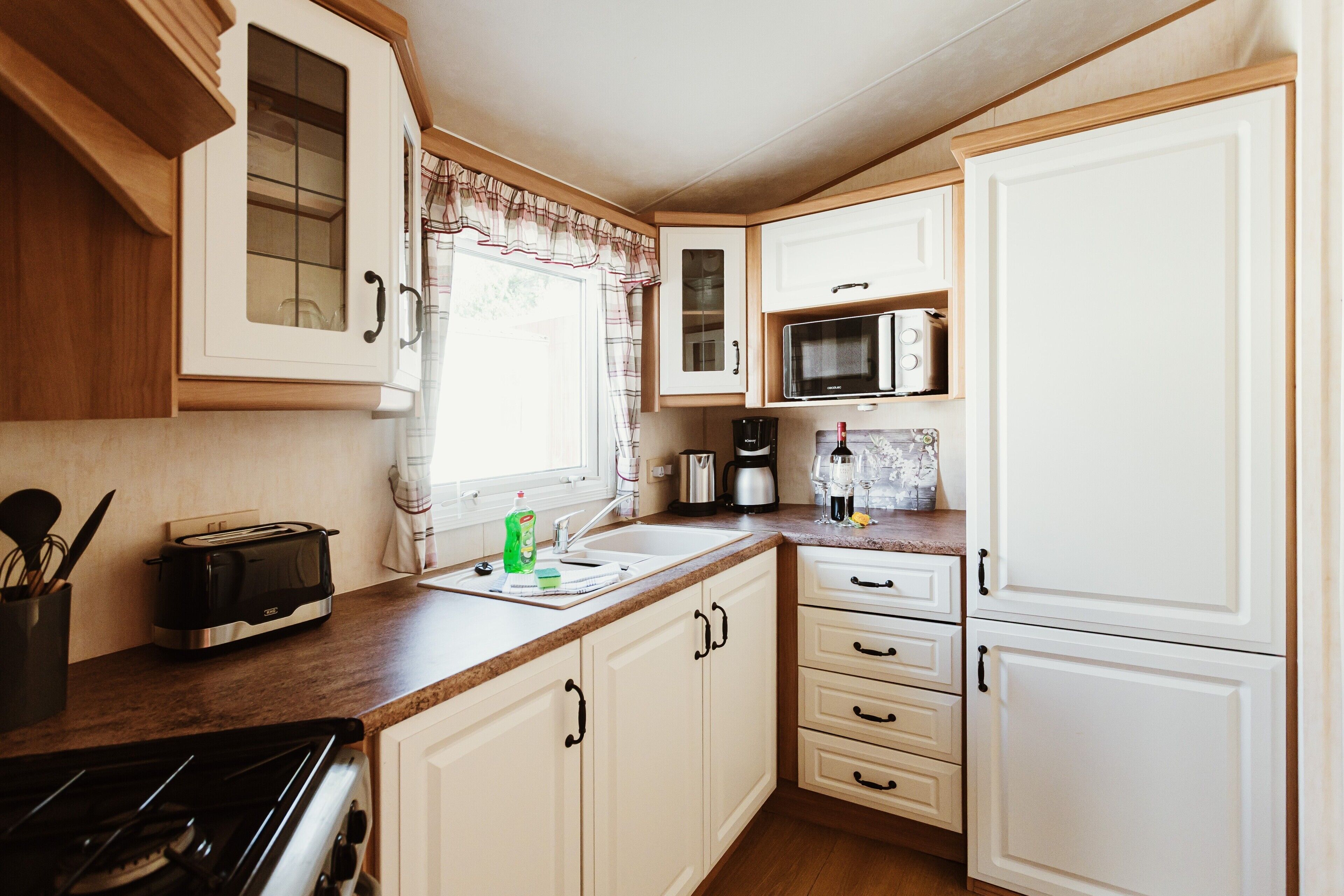 A compact kitchen with a stove, toaster, microwave, and white cabinets.