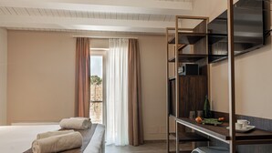 A hotel room with a bed, a desk with a TV, and a view of the outdoors through a window. - Manfredomus Farmhouse (Mussomeli)