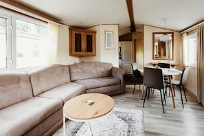 A living room with a sofa, a round coffee table, a dining area with chairs, a kitchen in the background, and a large window.
