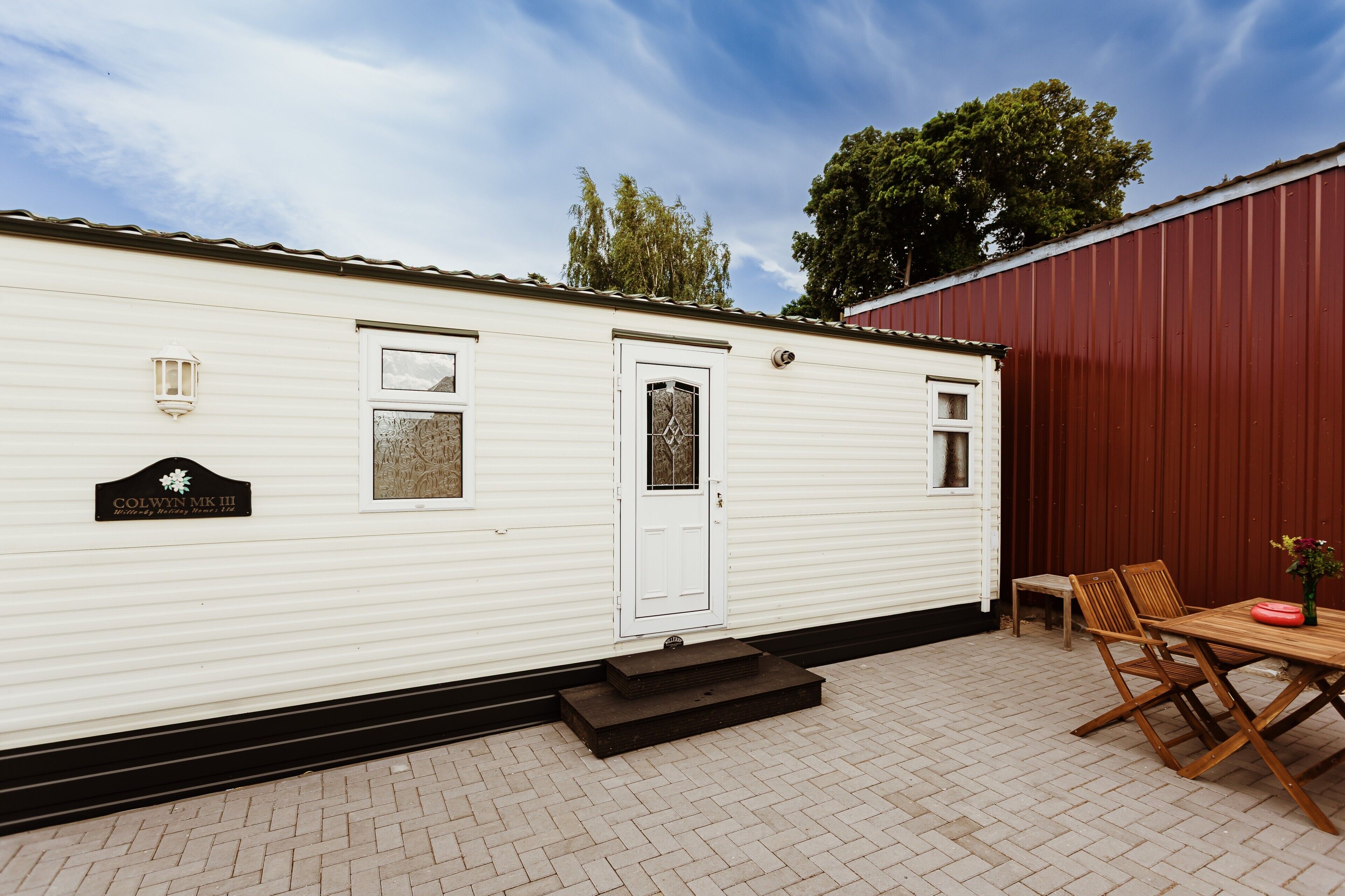 A mobile home with a white exterior, a front door, and a small porch area with a table and chairs.