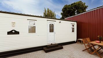 A mobile home with a white exterior, a front door, and a small porch area with a table and chairs.