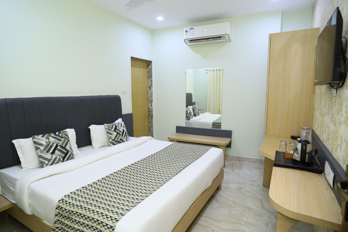 A hotel room with a bed, bedside table, mirror, and a TV mounted on the wall.