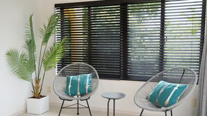 A room with two wicker chairs with cushions, a small round table, and a potted plant.
