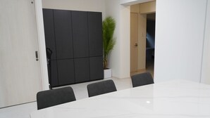 A conference room with a large white table, four chairs, a dark cabinet, and a potted plant.