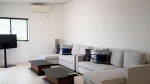 A modern living room with a sectional sofa, two coffee tables, a flat-screen TV, and a window with blinds.