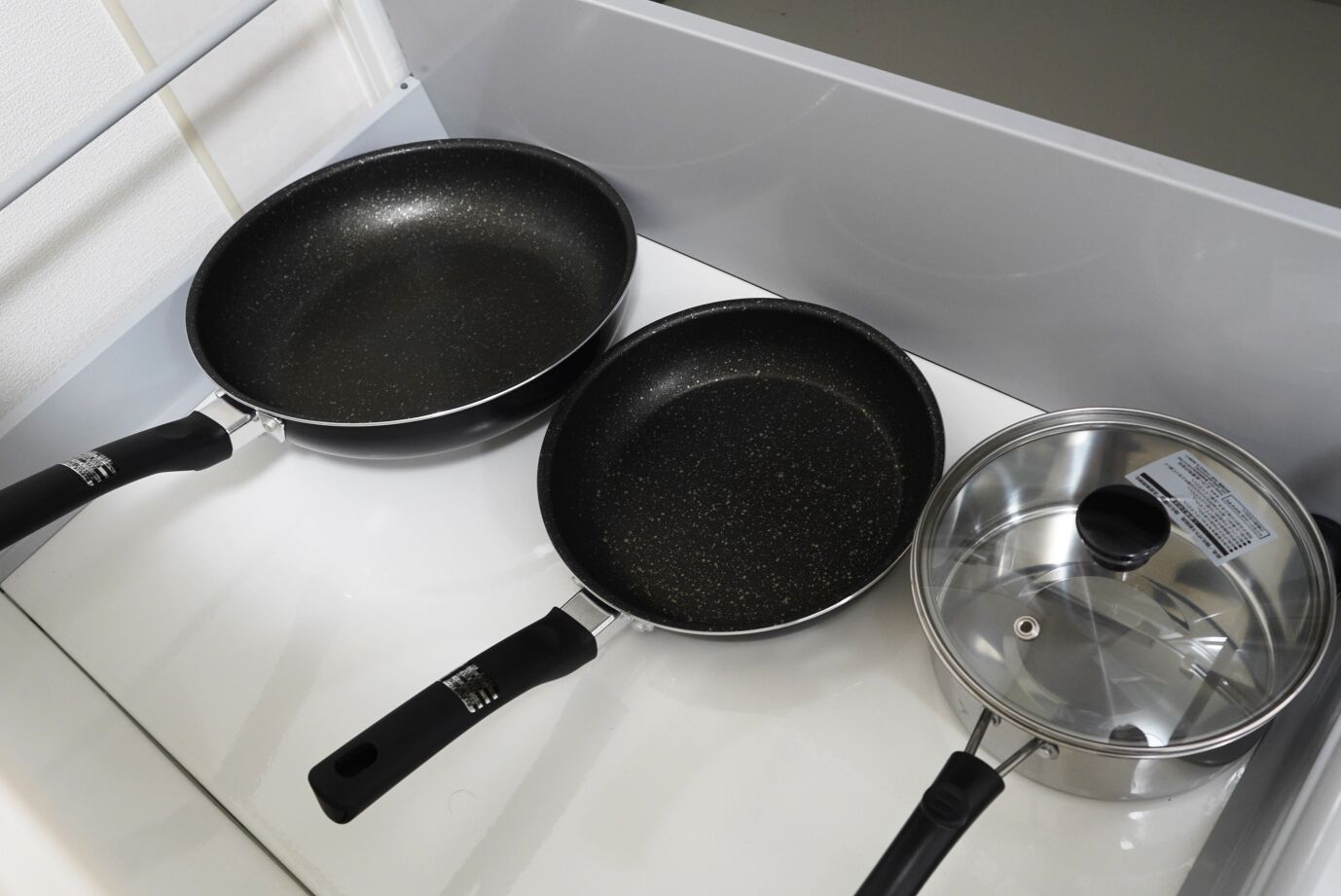 Trois poêles noires et une casserole en acier inoxydable sur une plaque de cuisson blanche.