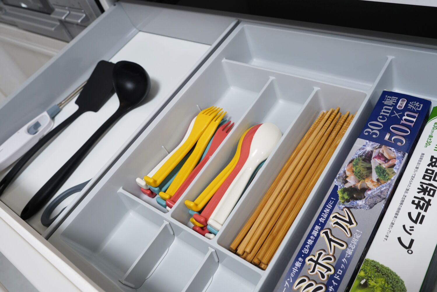 A drawer with compartments containing utensils, chopsticks, and a food packaging box.